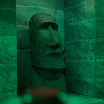 Statue moaï éclairée en vert derrière une vitre